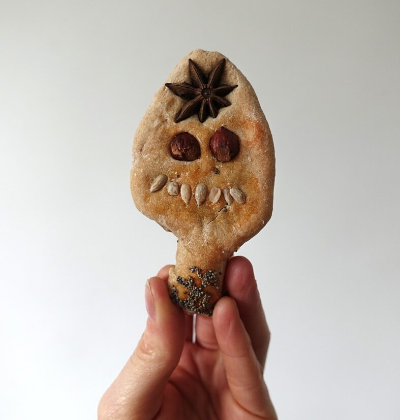pain en forme de tête, tenu par une main humaine. Des graines et des noix dessinent un visage : pavots, badiane, graines de tournesol et noisettes